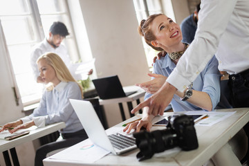 Happy designer people working together at desk on computer in office