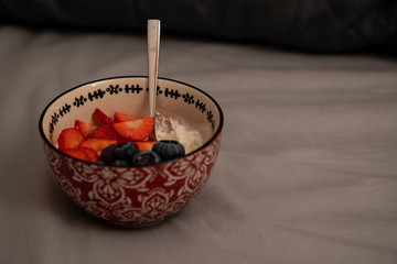 Top side view of a bowl with yogurt, strawberries and blueberries over grey sheets