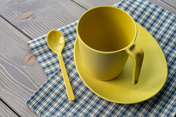 Yellow cup on a saucer with a spoon. Utensils of bamboo, with a checkered napkin on a wooden table. Shallow depth of field