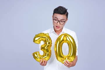 Asian young handsome attractive male student holding metallic foil balloon with number