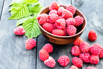 Ripe red raspberries on a bowl on the background of the old dark boards. Selective focus.