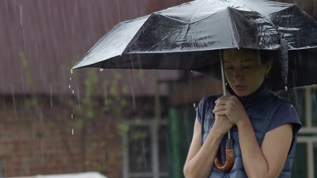 Stand under an umbrella in heavy rain. The girl is waiting for the rain to end. Hide from the rain under an umbrella