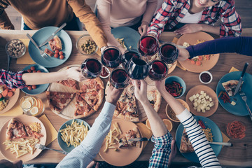 Cropped close up top above high angle photo company social crowd event hang out members buddies different race raise glasses beverage sit table shirts formal-wear sweaters pullovers loft room indoors