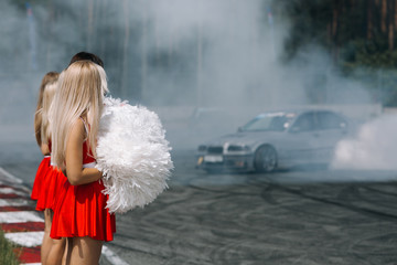 Grid girls is dancing at the race track and drift car make a lot of smoke at the back ground