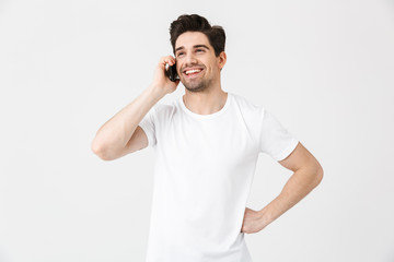 Happy young man posing isolated over white wall background talking by mobile phone.