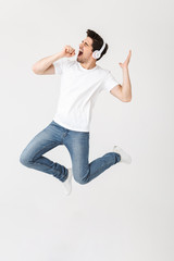Emotional excited young man posing isolated over white wall background listening music with headphones.