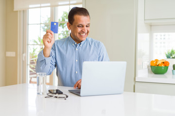 Naklejka na ściany i meble Middle age man showing credit card while using laptop