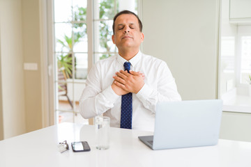 Middle age business man working with computer laptop smiling with hands on chest with closed eyes and grateful gesture on face. Health concept.