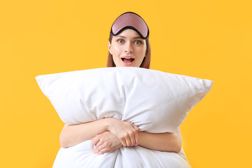 Surprised woman with pillow and sleep mask on color background
