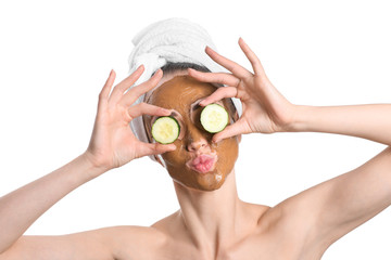 Beautiful young woman with facial mask and cucumber slices on white background