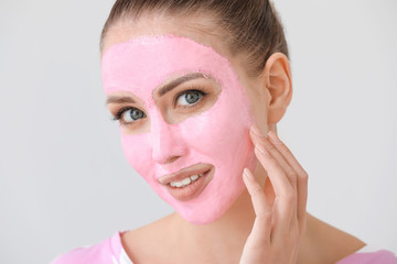 Beautiful young woman with facial mask on grey background