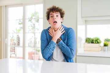 Young handsome man wearing casual denim jacket at home shouting and suffocate because painful strangle. Health problem. Asphyxiate and suicide concept.