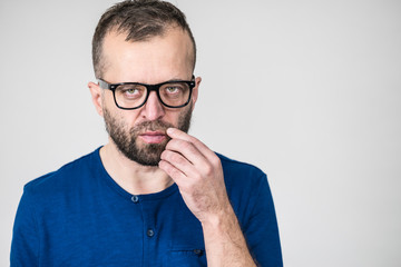 Adult clever guy wearing eyeglasses and blue shirt having thinking, focused face expression. Man focusing on his work, contemplating idea.