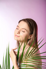 Naklejka premium Young woman with closed eyes and green palm leaf, natural beauty and skincare concept, wellness and relaxation