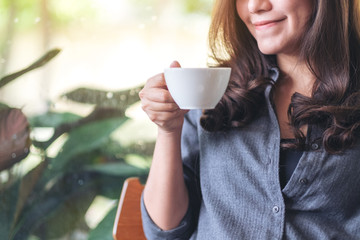 Closeup image of a beautiful woman holding and drinking hot coffee in cafe