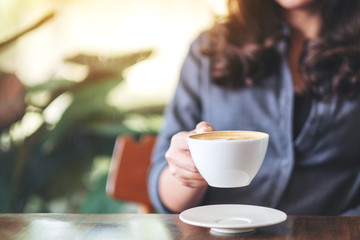 Closeup image of a woman holding and drinking hot coffee in cafe