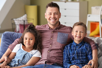 Happy man with little adopted children sitting on sofa at home