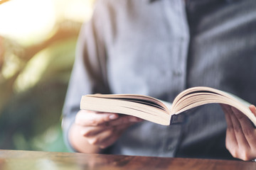 Closeup image of a woman holding and reading a vintage novel book on wooden table
