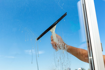 Washing cleaning windows by cleaning service hand with a special brush squeegee window cleaner on a blue sky background