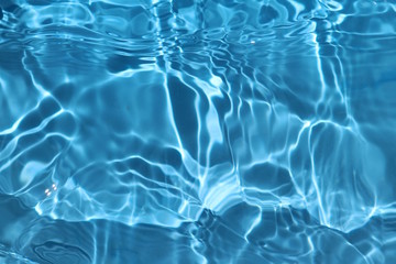Blue and bright water surface with sun refection in swimming pool for background 