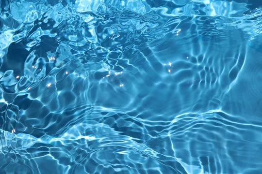 Blue and bright water surface with sun refection in swimming pool for background 