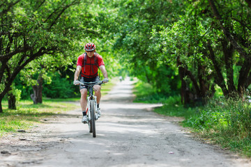 Obraz premium young man on mountain bike on sunny day ride in park, dressed red sportswear
