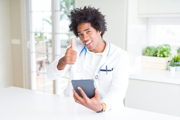 African American doctor man using tablet at the clinic happy with big smile doing ok sign, thumb up with fingers, excellent sign