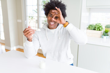 African American man eating healthy yogurt for breakfast with happy face smiling doing ok sign with...
