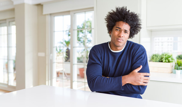 Young african american man wearing casual sweater sitting at home shaking and freezing for winter cold with sad and shock expression on face
