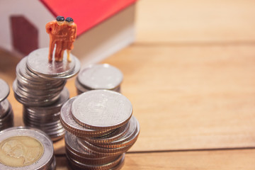 Miniature family stand with coins house and car on wooden table. family planning concept.