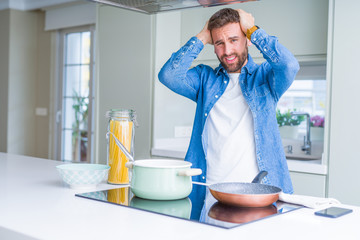 Handsome man cooking italian spaghetti pasta at the kitchen suffering from headache desperate and stressed because pain and migraine. Hands on head.