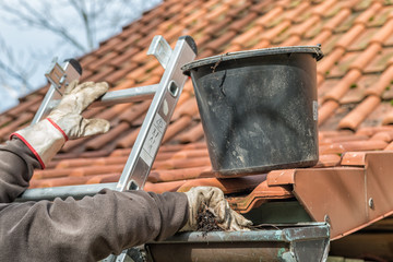 Man on a ladder cleaning house gutters © Zerbor