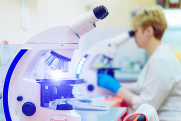 Modern microscopes and a laboratory specialist is looking at one of them indoors. Microscope plate...