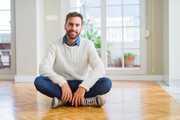Handsome man wearing casual sweater sitting on the floor at home with a happy and cool smile on...