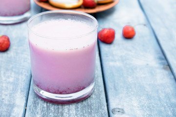 Cocktail with milk and berries club in a glass against the background of blue boards.
