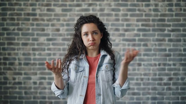 Portrait of surprised young woman sighing and gesturing after unpleasant surprise standing on brick wall background. Negative emotions, fear and unhappy youth concept.