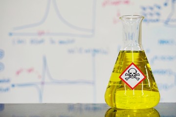 Erlenmeyer flask with Yellow liquid and chemical hazard warning symbols labels (acute toxicity symbol) on whiteboard with chemical learning background.