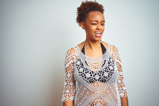Young african american woman with afro hair wearing a bikini over white isolated background winking looking at the camera with sexy expression, cheerful and happy face.