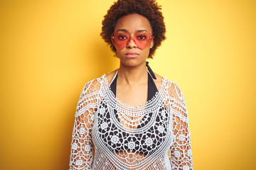 Young african american woman with afro hair wearing bikini and heart shaped sunglasses with serious expression on face. Simple and natural looking at the camera.