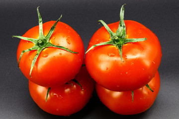 Two tomatoes lie on two other tomatoes, black background