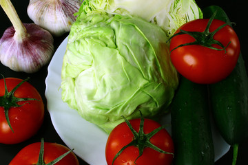 On the black background are - young and early garlic, red tomatoes, cabbage, two green cucumbers, long and large