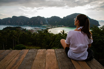 Beautiful woman sitting on wooden platform with Phi Phi island views and cloudy sky