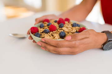 Close up of young woman eating healthy cereals and berries for breakfast