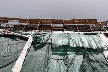 new building hidden behind scaffolding and protective net (veil). Construction scaffolding of a building under renovation. House facade for restore, repair and renovate.