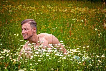 Junger Mann liegt mit nacktem Oberkörper in einer Blumenwiese