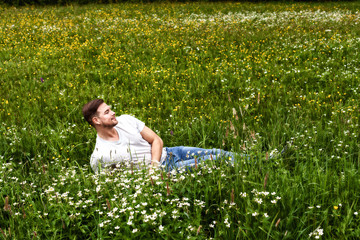 Junger Mann mit Bart liegt in einer Bergwiese und genießt den Duft der Blumen.