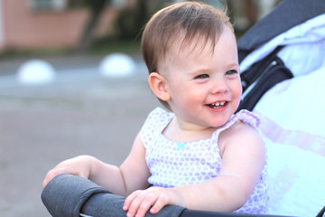 little, beautiful, smiling, cute redhead baby in a pram out-of-doors in a sleeveless shirt