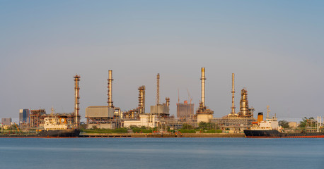 Crude oil refinery plant and many chimney with petrochemical tanker or cargo ship at coast of river on sky afternoon  bright day at thailand