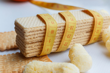 yellow plastic measuring tape girds two waffles, cookies, sweet corn sticks in the background. dietary for slim shape, dependence on sugary flour products that lead to obesity and digestive problems.
