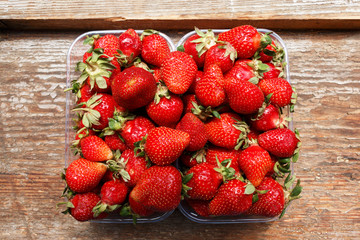 fresh and ripe organic strawberries in plastic containers lying on an old rustic wooden window background. strawberry harvest.